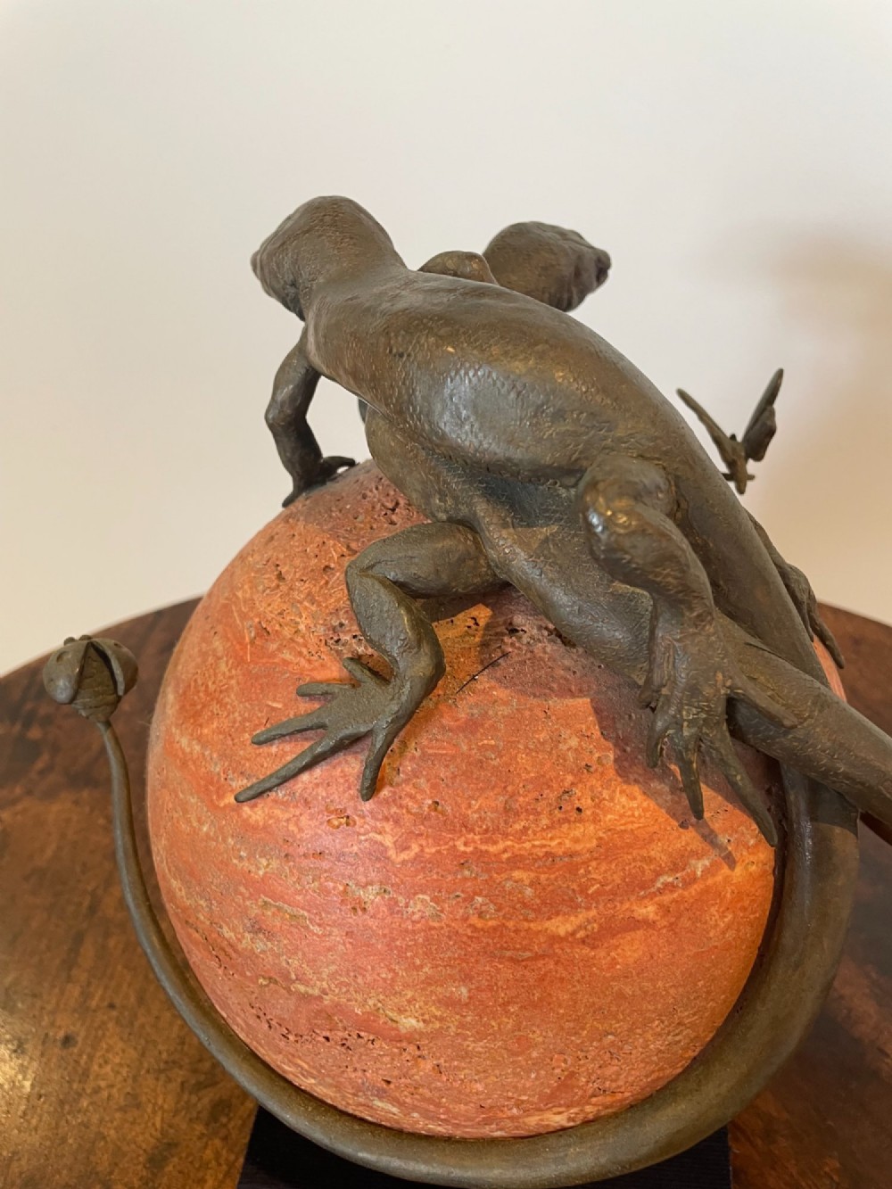 A dark bronze sculpture depicting two realistic lizards perched on top of a spherical red veined marble base. View X