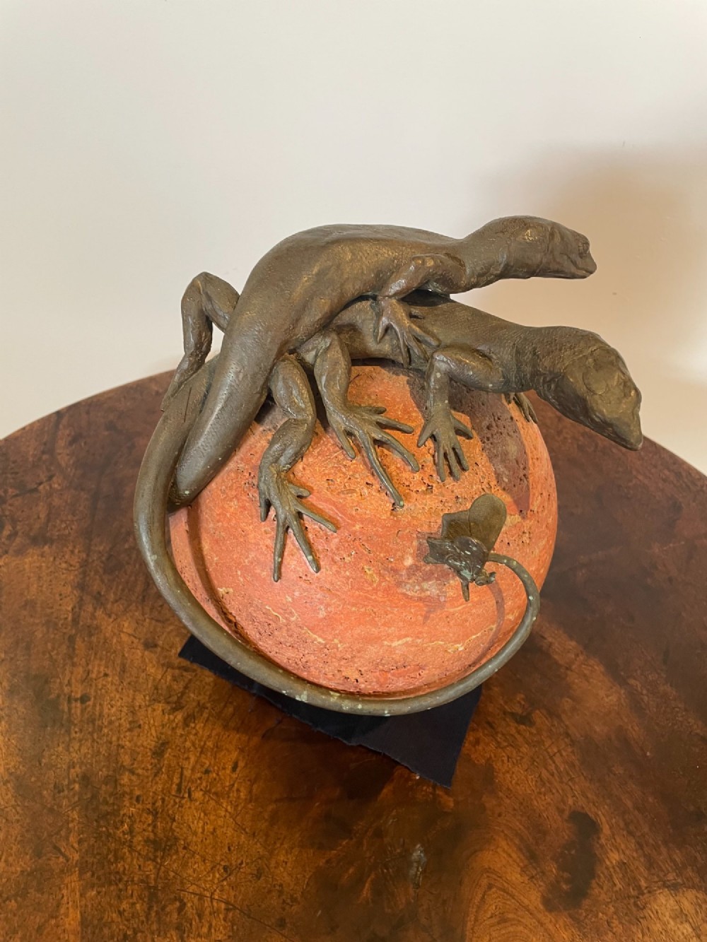 A dark bronze sculpture depicting two realistic lizards perched on top of a spherical red veined marble base. View XI