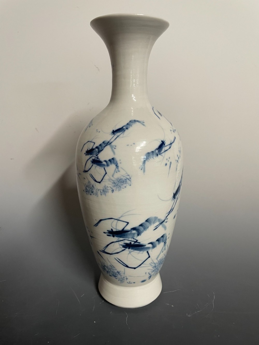A tall white porcelain vase with a flared rim, featuring hand-painted cobalt blue shrimp motifs around the body.