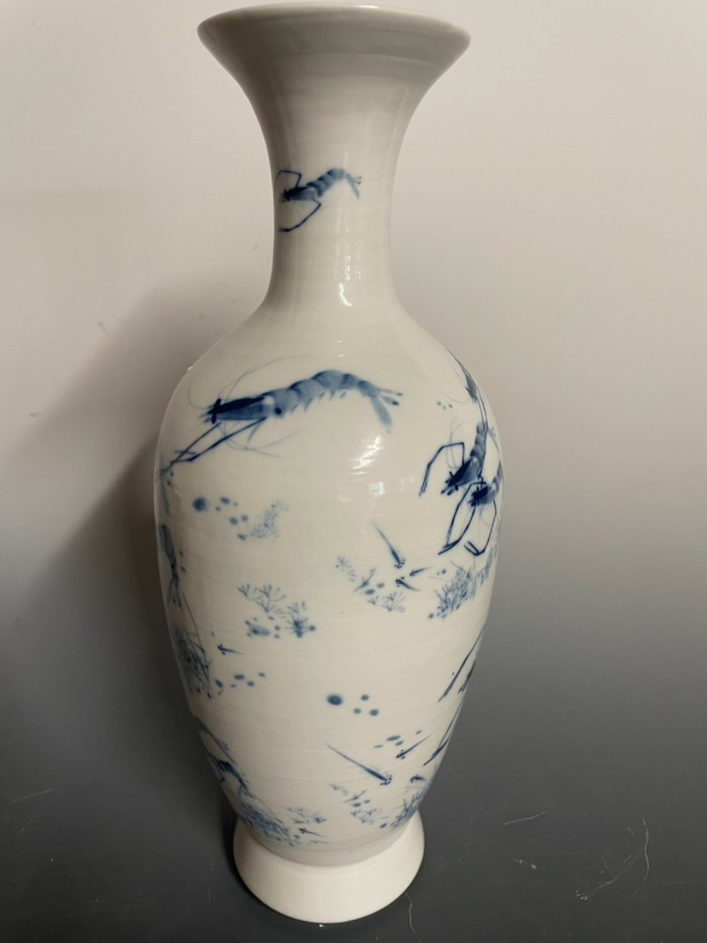 A tall white porcelain vase with a flared rim, featuring hand-painted cobalt blue shrimp motifs around the body. View V