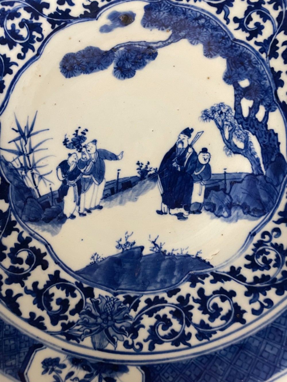 A circular Chinese porcelain plate decorated with underglaze cobalt blue figures beneath a pine tree within floral and geometric patterned borders. View II