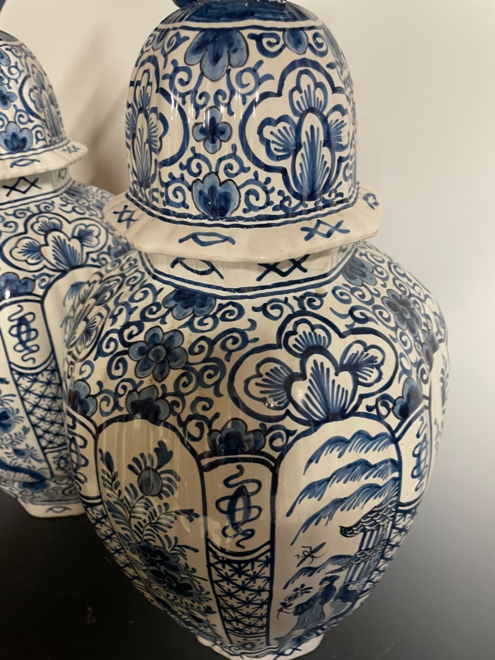 A pair of blue and white tin-glazed earthenware ribbed jars with lidded covers topped with foo dog finials, decorated with hand-painted chinoiserie scenes. View IV