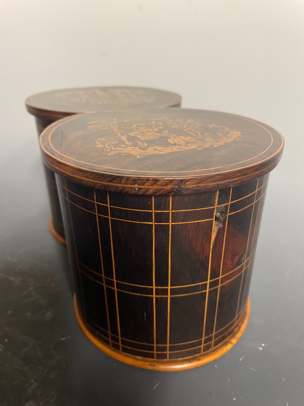 A dark brown wooden double cylindrical tea caddy featuring geometric line inlay and detailed figural marquetry scenes on the lids. View II