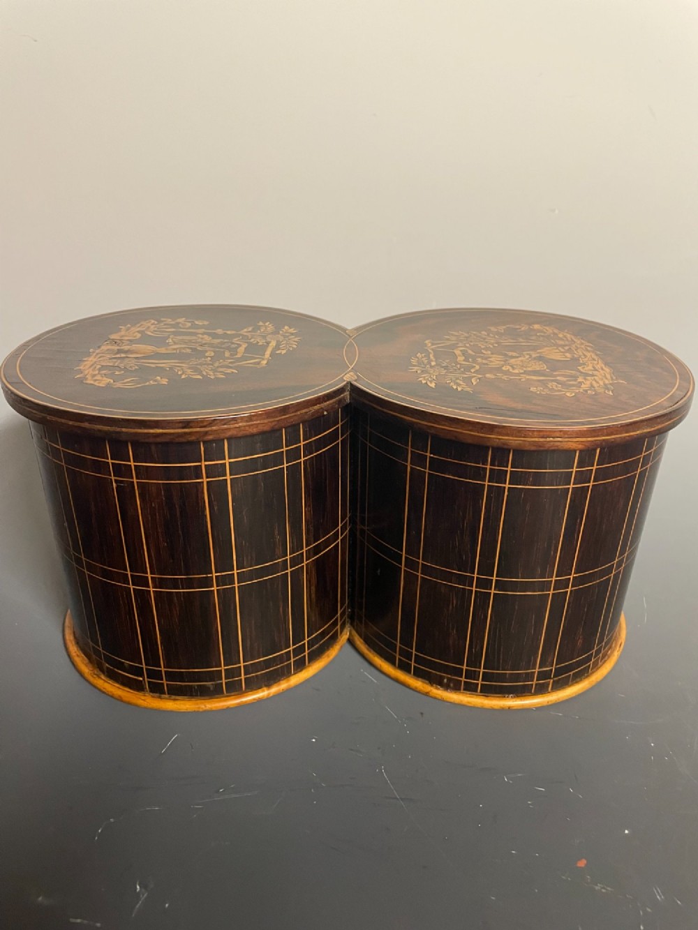 A dark brown wooden double cylindrical tea caddy featuring geometric line inlay and detailed figural marquetry scenes on the lids. View III