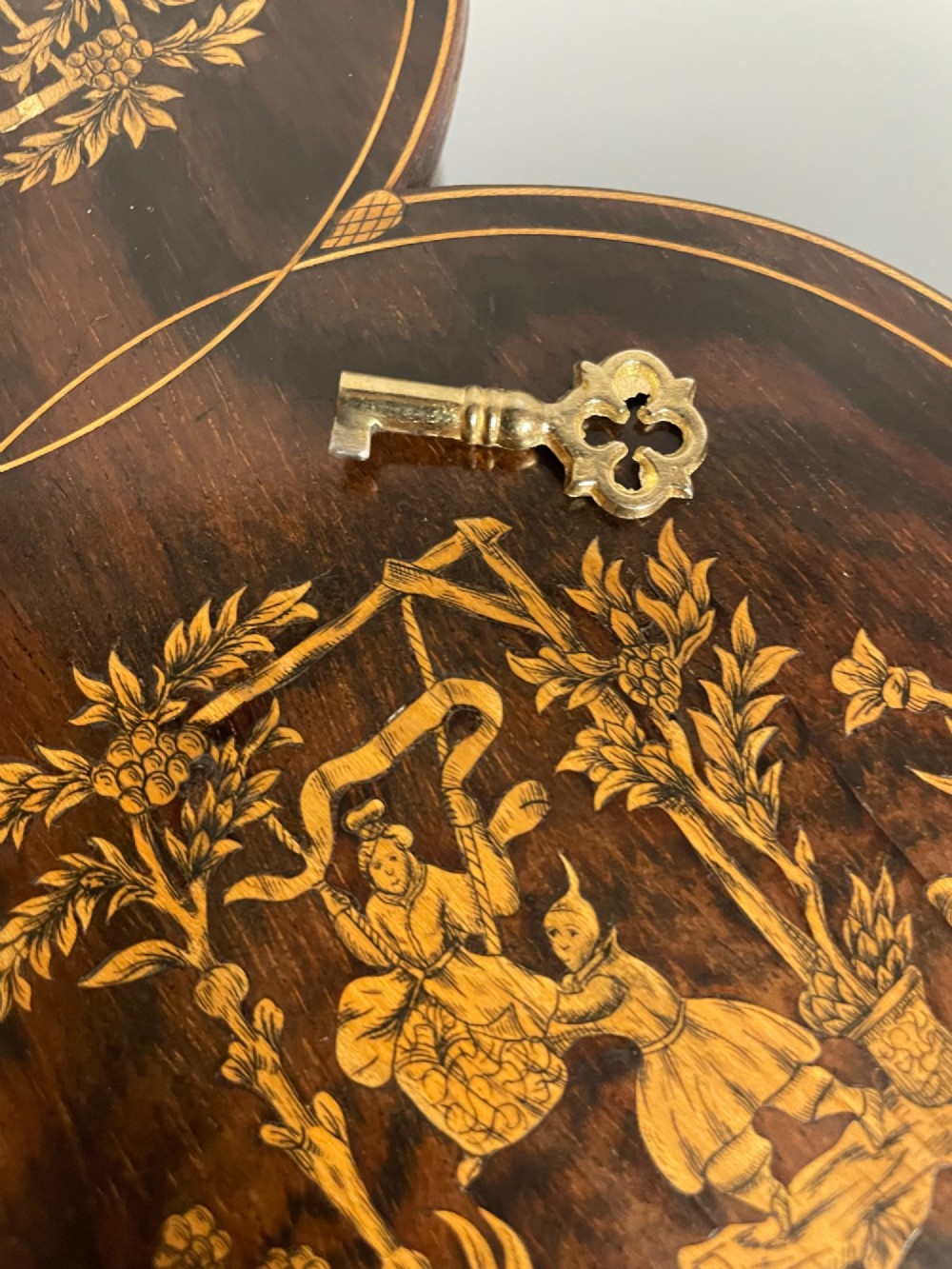 A dark brown wooden double cylindrical tea caddy featuring geometric line inlay and detailed figural marquetry scenes on the lids. View XIV