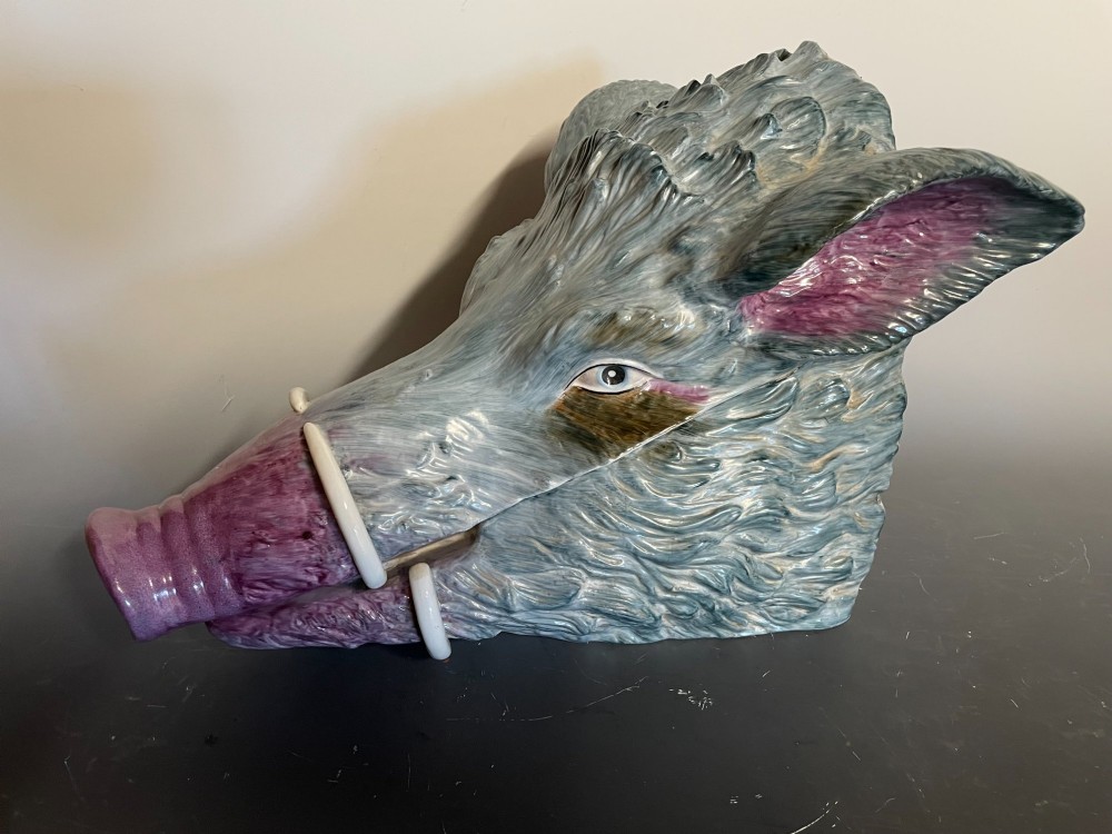 A glazed ceramic majolica tureen sculpted in the shape of a boars head with grey textured fur, pink snout, and white tusks.