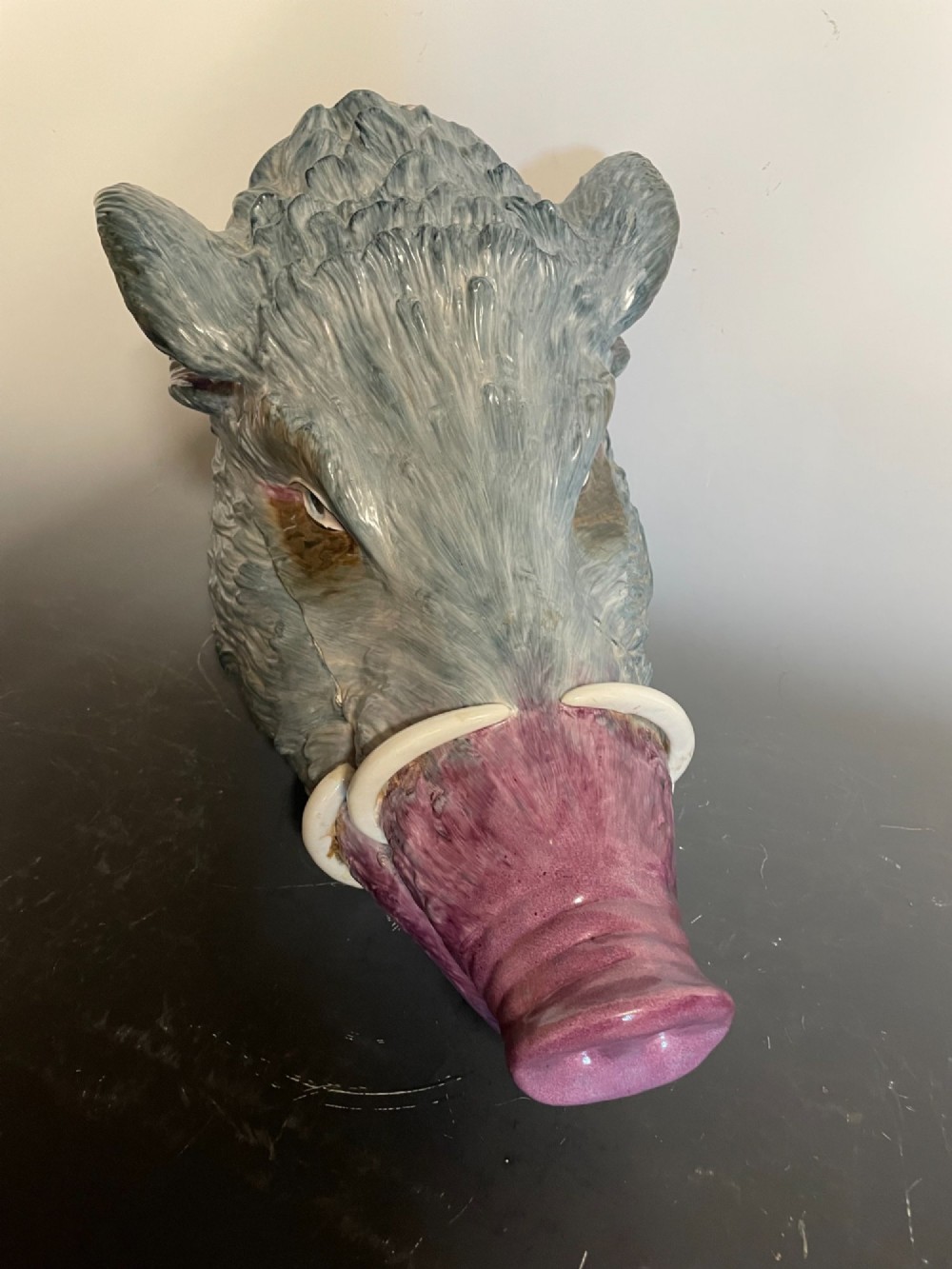A glazed ceramic majolica tureen sculpted in the shape of a boars head with grey textured fur, pink snout, and white tusks. View V