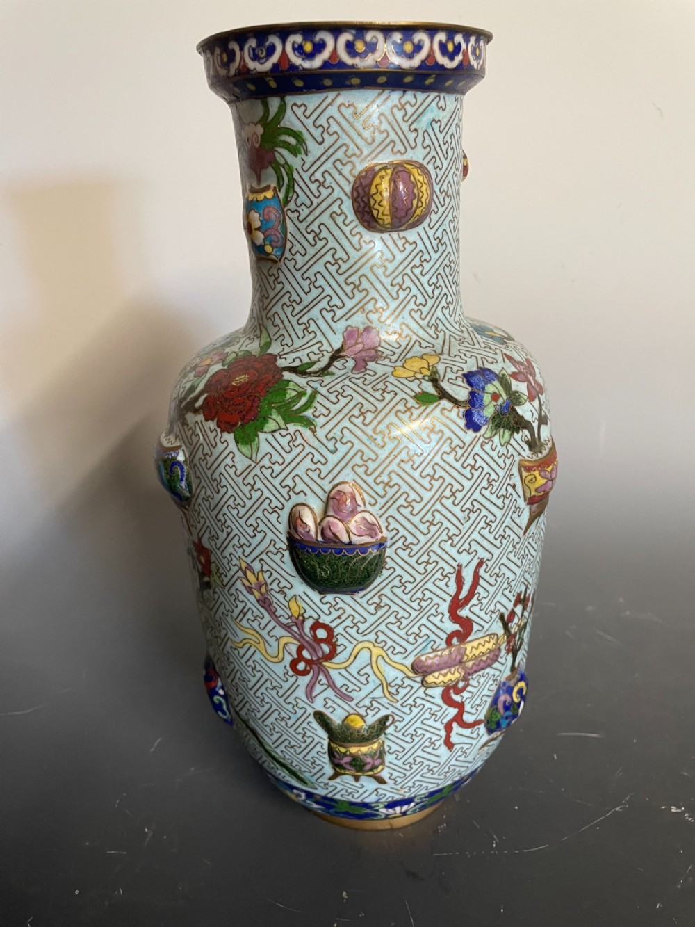 A baluster-shaped Chinese cloisonne enamel vase featuring a light blue key fret background embellished with colourful scholars objects and floral motifs. View IV