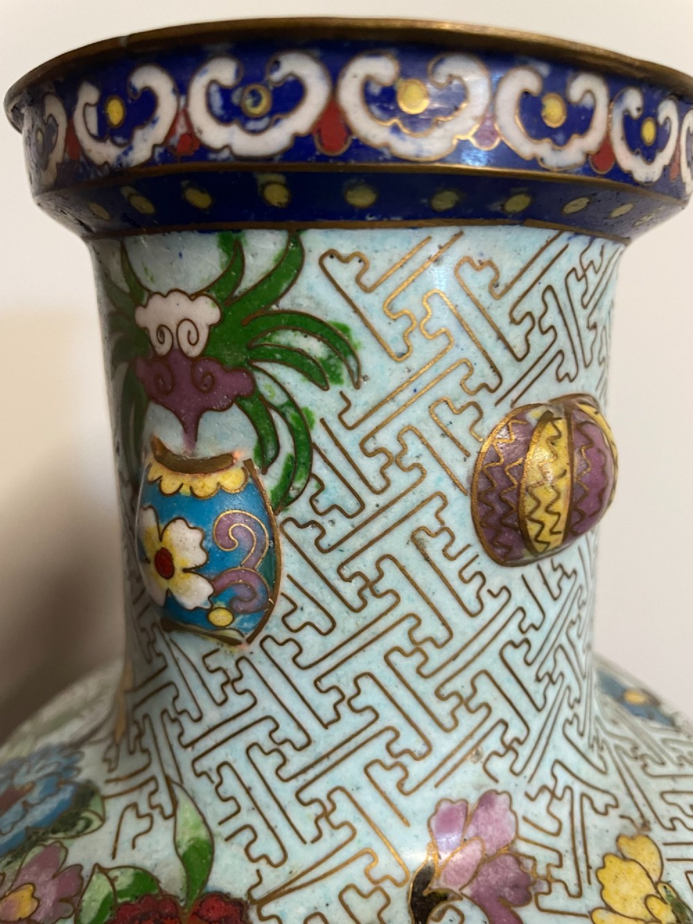 A baluster-shaped Chinese cloisonne enamel vase featuring a light blue key fret background embellished with colourful scholars objects and floral motifs. View IX