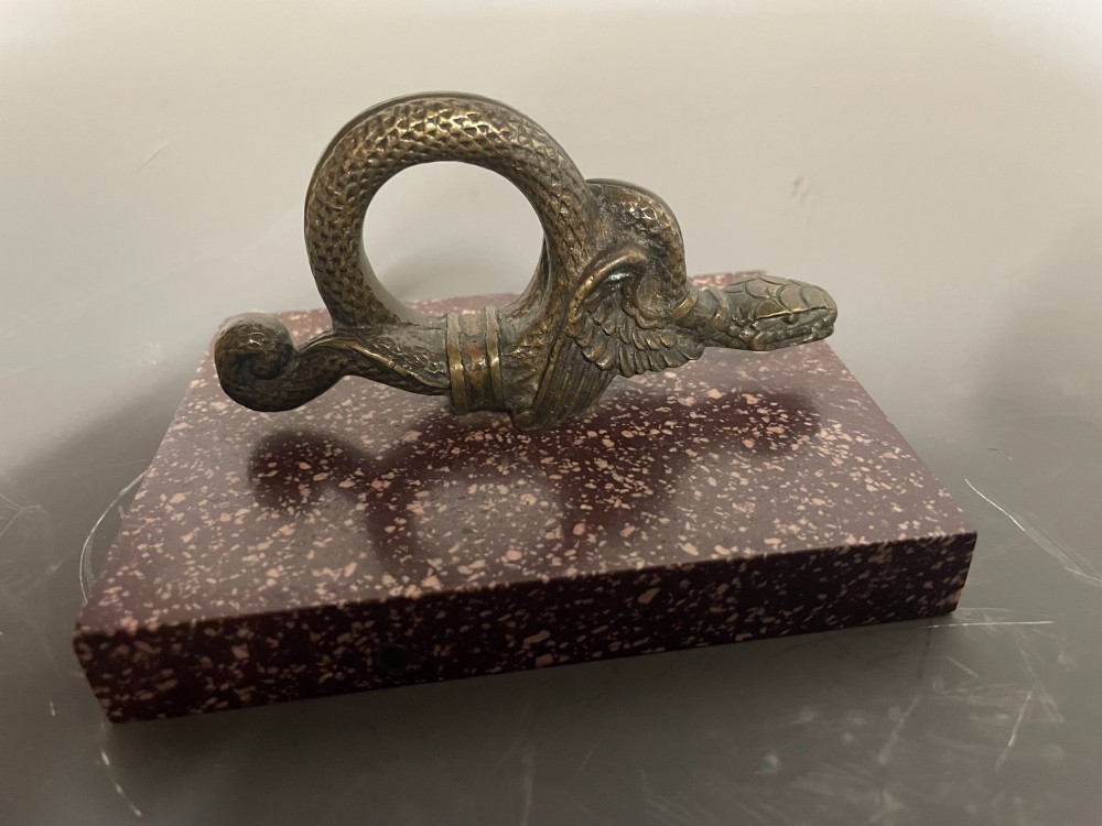 A cast bronze winged serpent sculpture mounted on a rectangular speckled red marble base.