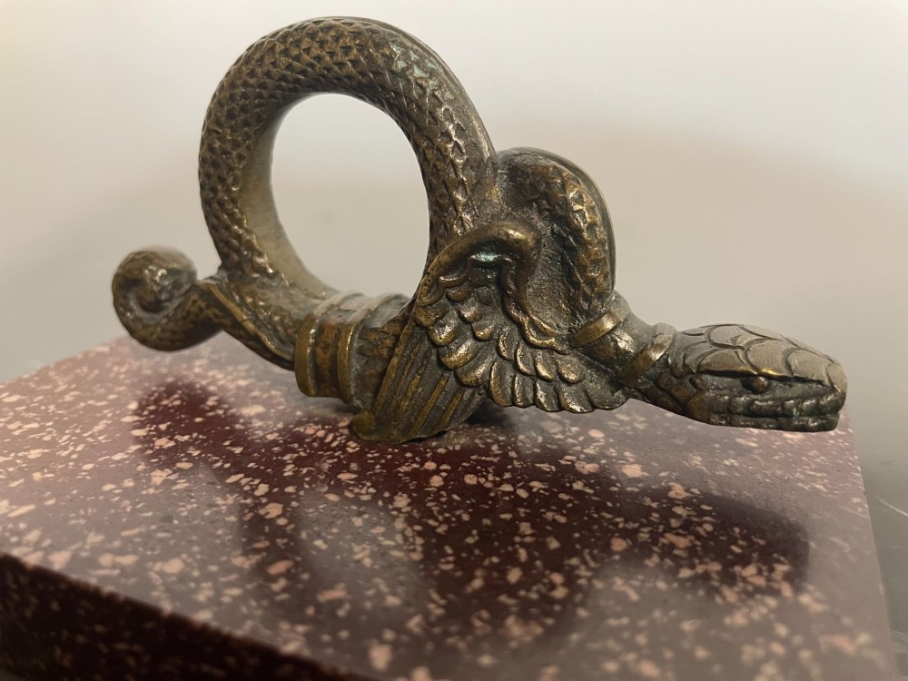 A cast bronze winged serpent sculpture mounted on a rectangular speckled red marble base. View II