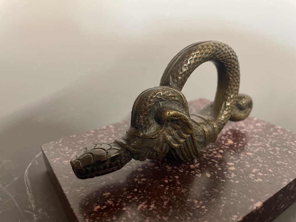 A cast bronze winged serpent sculpture mounted on a rectangular speckled red marble base. View IV