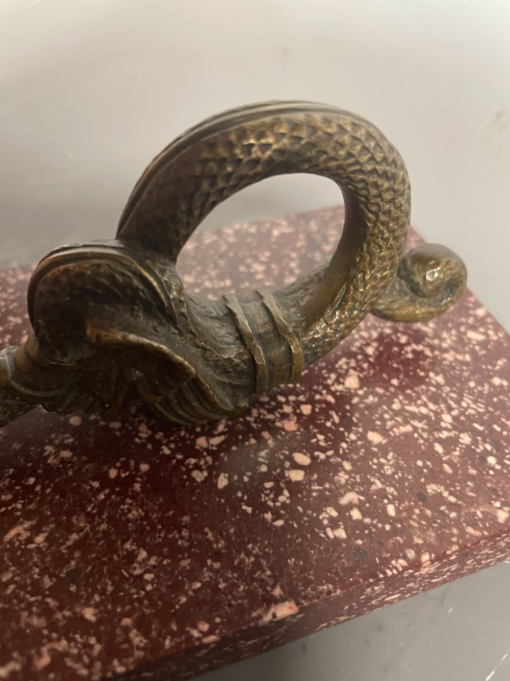 A cast bronze winged serpent sculpture mounted on a rectangular speckled red marble base. View V