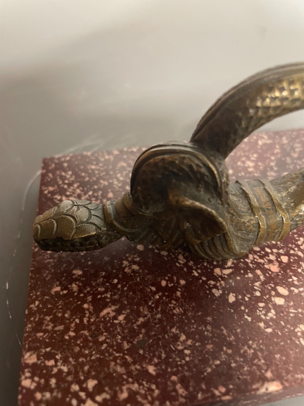 A cast bronze winged serpent sculpture mounted on a rectangular speckled red marble base. View VI