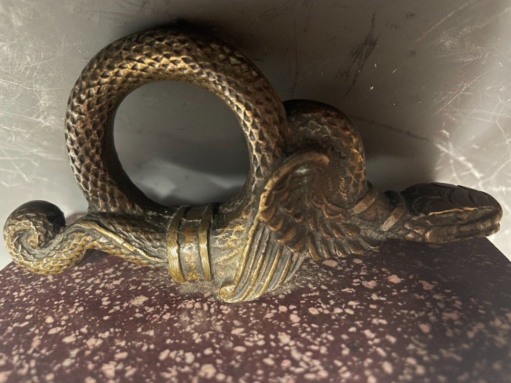 A cast bronze winged serpent sculpture mounted on a rectangular speckled red marble base. View VII