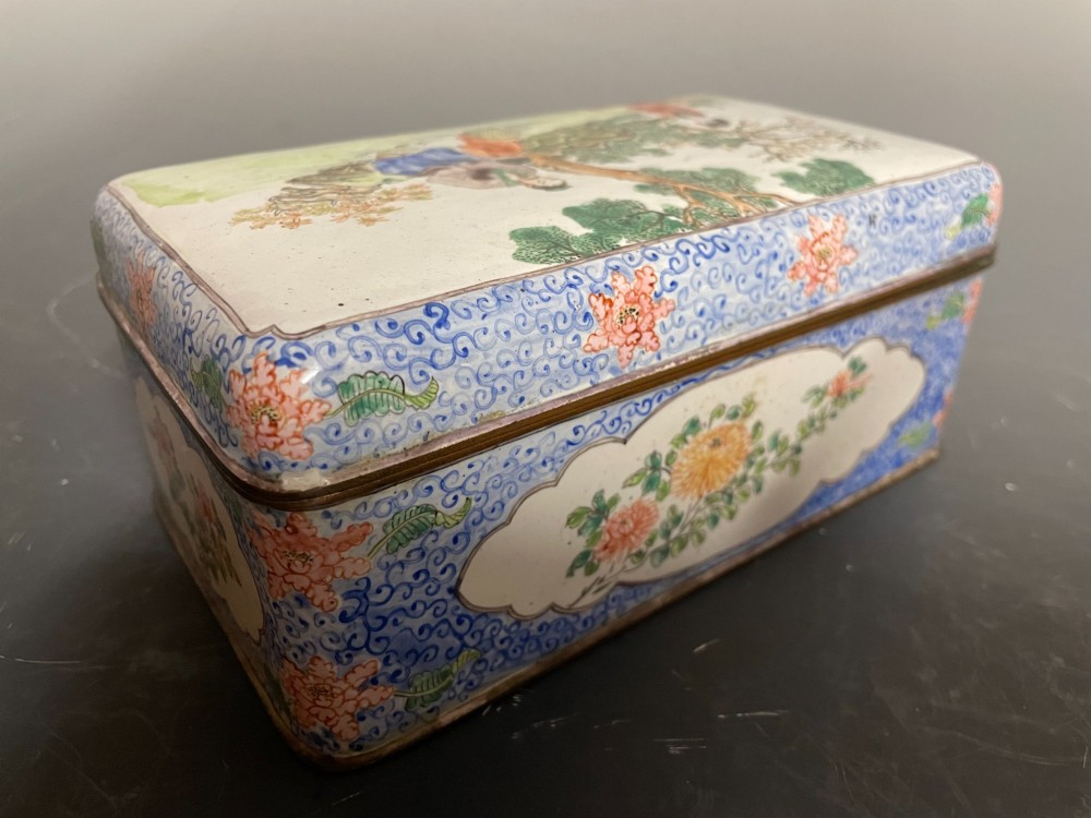 A rectangular Chinese Canton enamel box with rounded corners featuring hand-painted figures in a landscape setting on the lid and floral scrollwork on the side. View IV