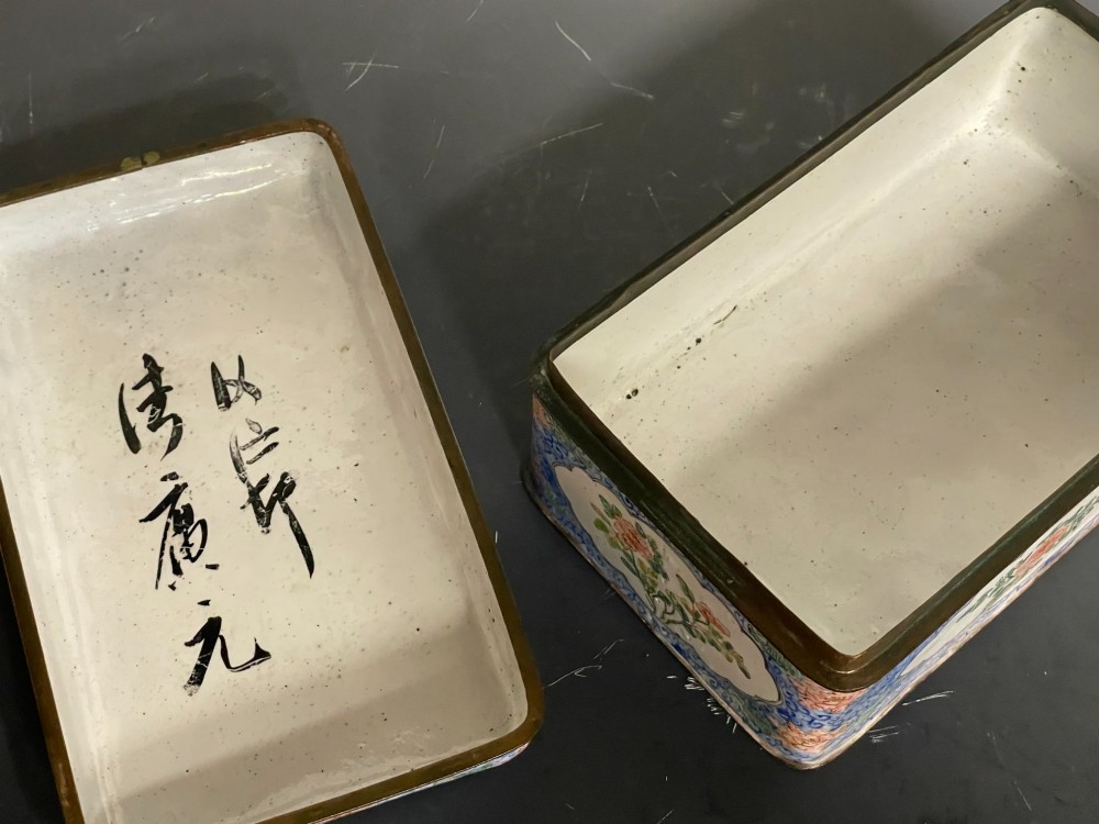 A rectangular Chinese Canton enamel box with rounded corners featuring hand-painted figures in a landscape setting on the lid and floral scrollwork on the side. View VI