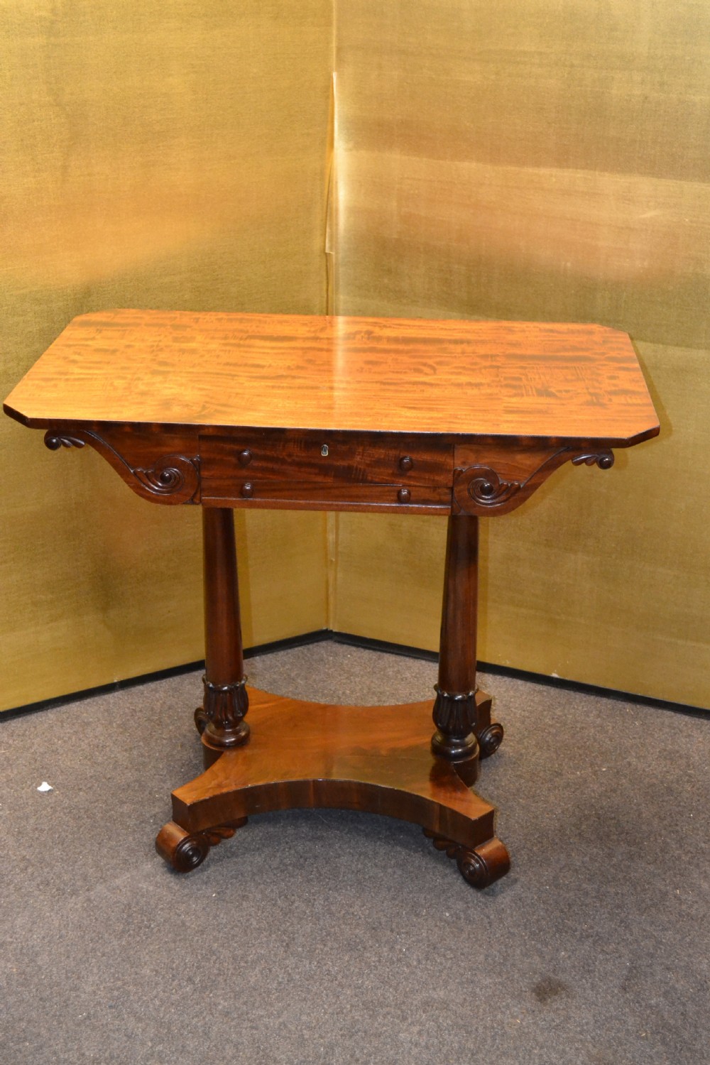 A William IV mahogany side table featuring carved scroll brackets, twin turned column supports, and a shaped plinth base on scroll feet.