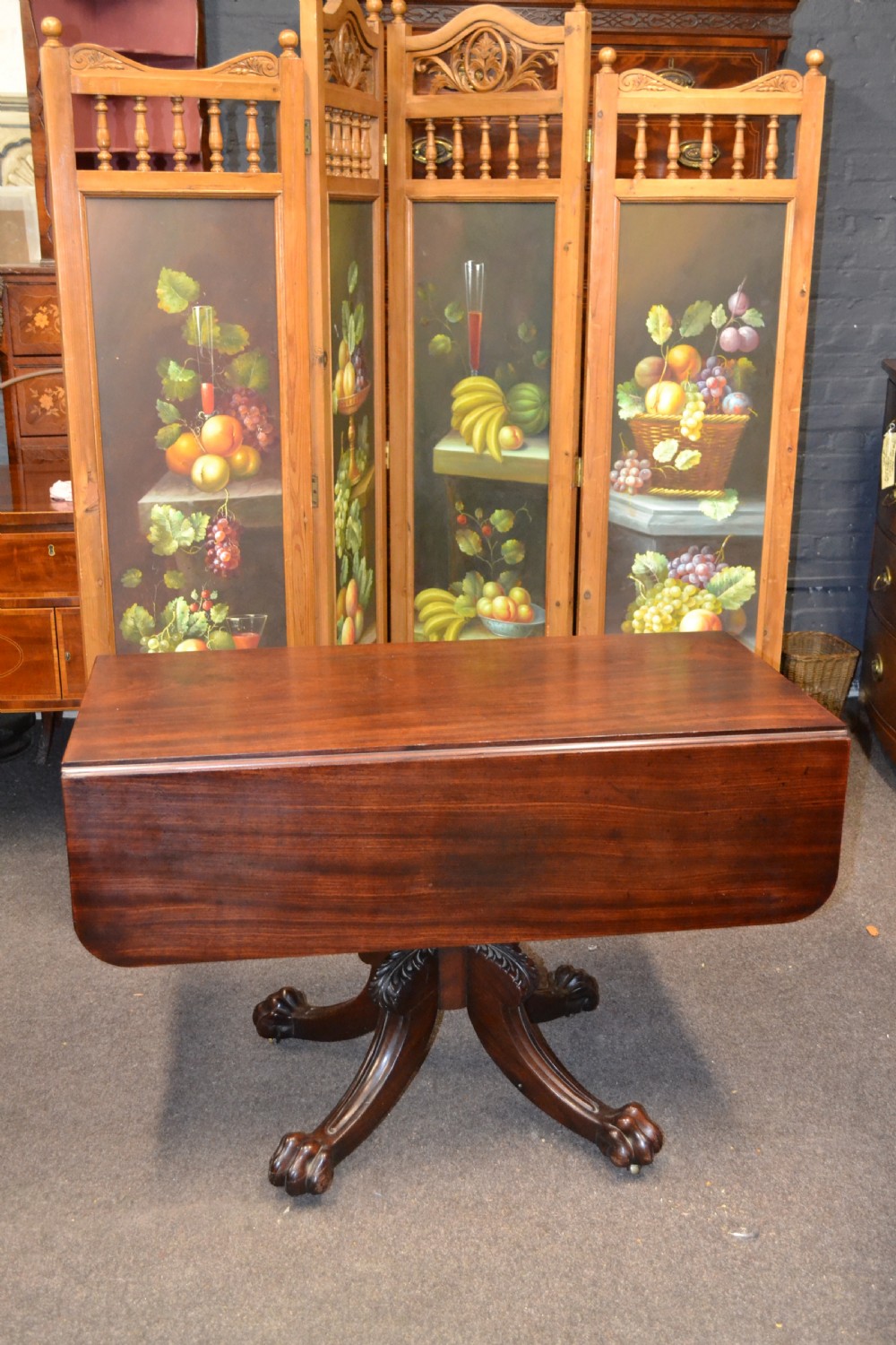 An antique mahogany Pembroke table featuring hinged drop leaves, supported by a central carved pedestal with four splayed legs ending in carved feet.