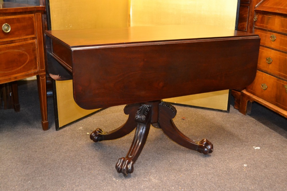 An antique mahogany Pembroke table featuring hinged drop leaves, supported by a central carved pedestal with four splayed legs ending in carved feet. View II