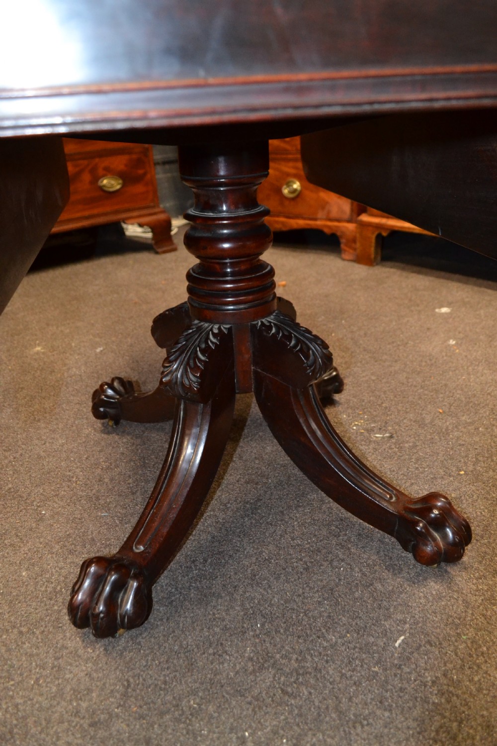 An antique mahogany Pembroke table featuring hinged drop leaves, supported by a central carved pedestal with four splayed legs ending in carved feet. View III