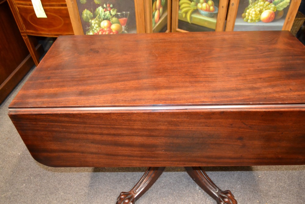 An antique mahogany Pembroke table featuring hinged drop leaves, supported by a central carved pedestal with four splayed legs ending in carved feet. View VII