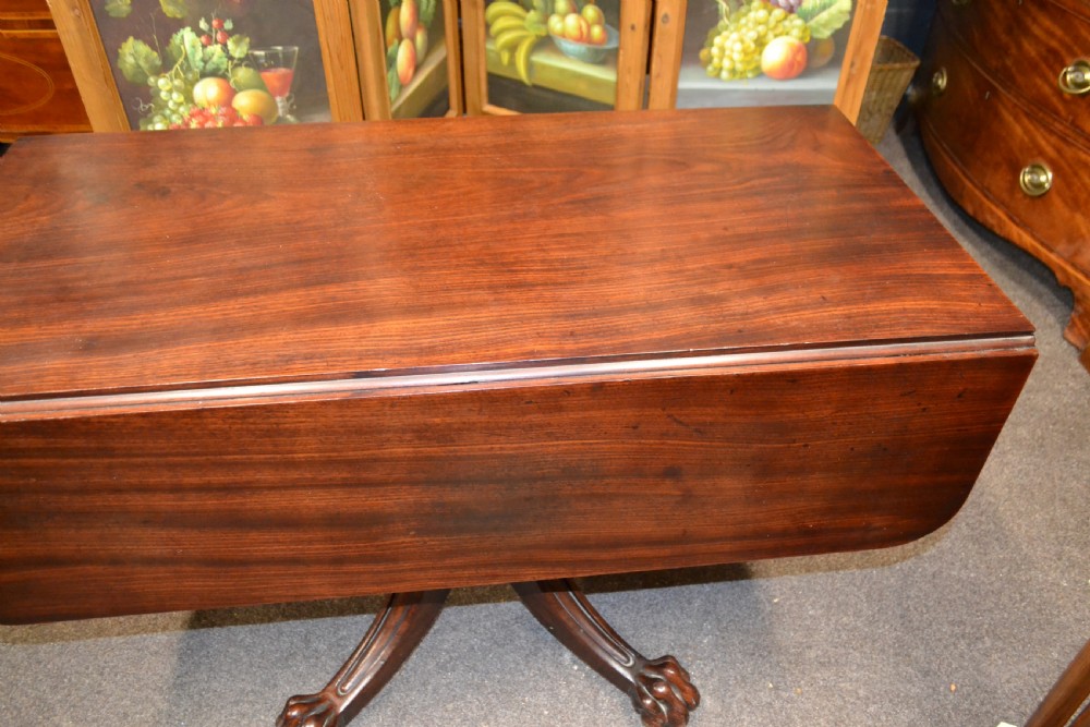An antique mahogany Pembroke table featuring hinged drop leaves, supported by a central carved pedestal with four splayed legs ending in carved feet. View VIII