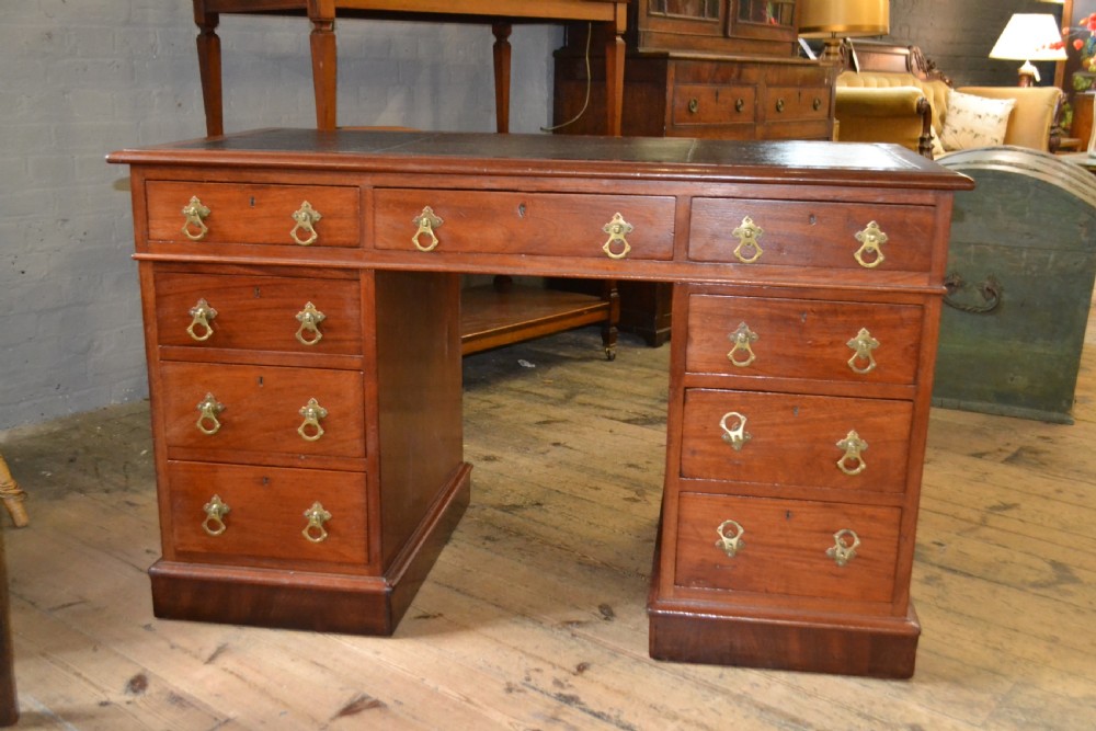 A Victorian walnut pedestal desk featuring nine drawers with brass handles and a dark leather writing insert.