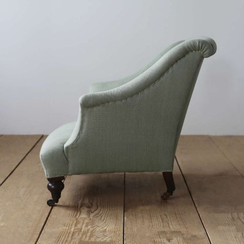 A 19th-century Victorian armchair upholstered in sage green fabric, featuring sloping arms and dark turned wooden front legs with castors. View III
