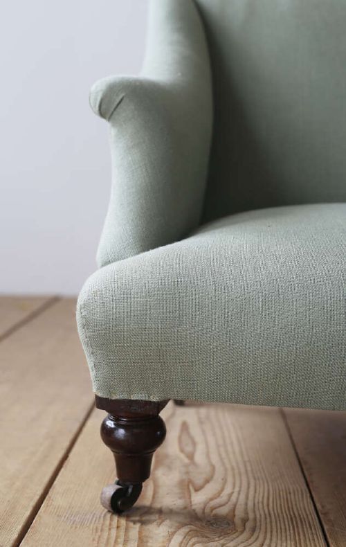 A 19th-century Victorian armchair upholstered in sage green fabric, featuring sloping arms and dark turned wooden front legs with castors. View IV
