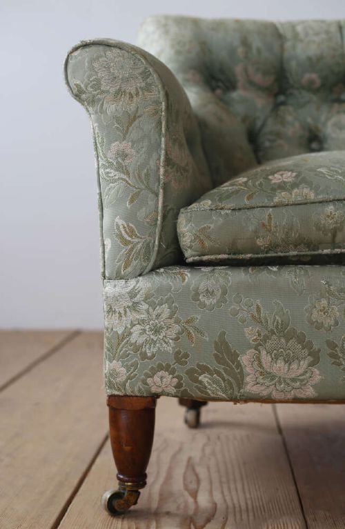 A 19th-century upholstered armchair featuring sage green floral damask fabric, deep button-tufting on the backrest, turned wood front legs, and brass castors. View II