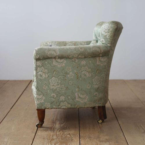 A 19th-century upholstered armchair featuring sage green floral damask fabric, deep button-tufting on the backrest, turned wood front legs, and brass castors. View IV