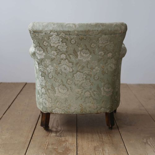A 19th-century upholstered armchair featuring sage green floral damask fabric, deep button-tufting on the backrest, turned wood front legs, and brass castors. View V