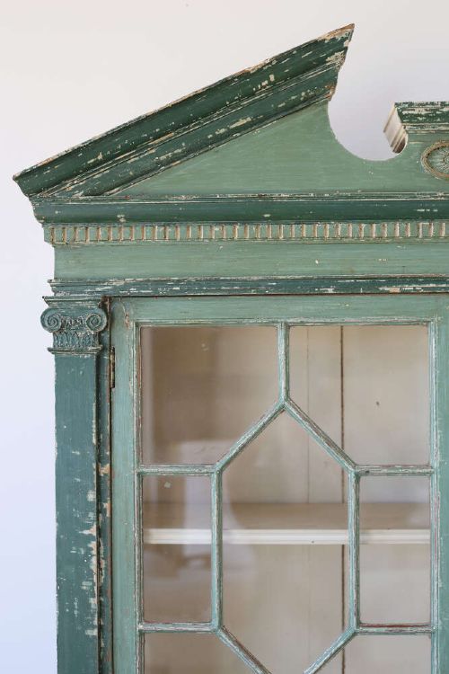 A 19th-century distressed green painted glazed bookcase featuring a broken pediment, astragal glazing doors, and open lower cubby compartments. View II
