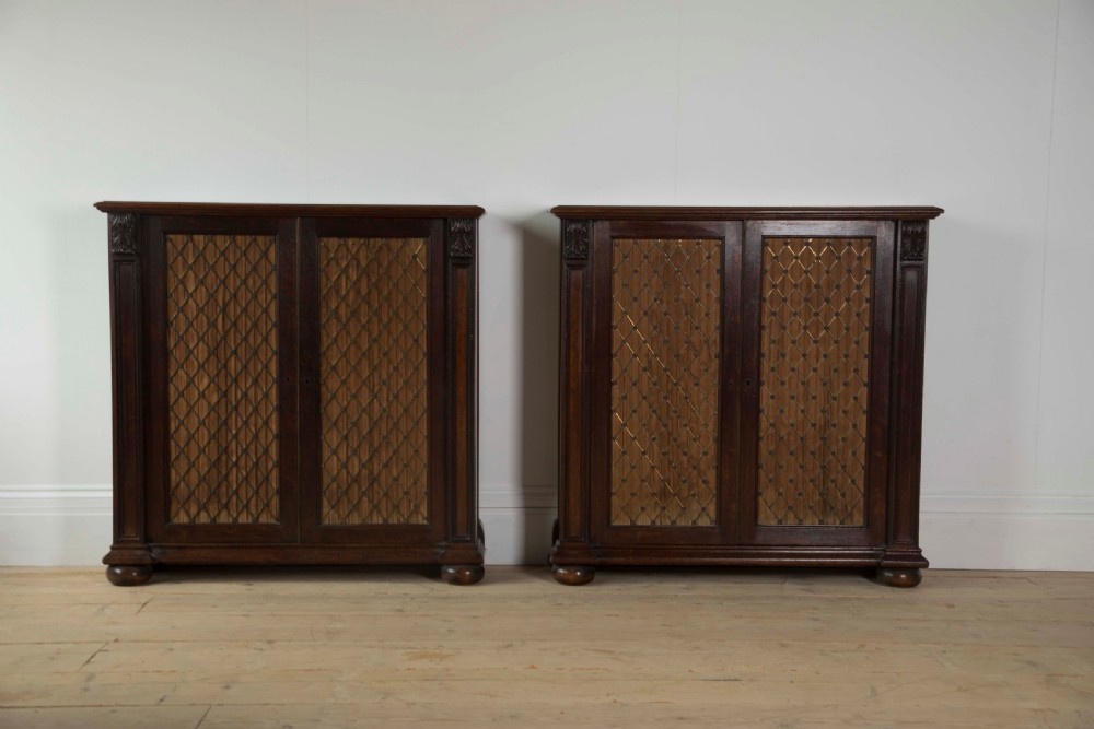 A pair of matching dark mahogany low cabinets featuring double doors with brass diamond wire grilles and carved corner accents.