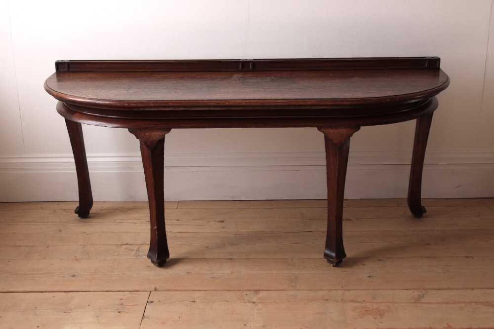 A 19th-century dark wood demi-lune table featuring a semicircular top, a low rear gallery edge, and four shaped legs.
