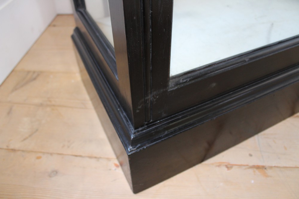 A tall, narrow black painted wooden display cabinet featuring glass side and front panels, interior glass shelves, a moulded cornice, and brass latch hardware. View III
