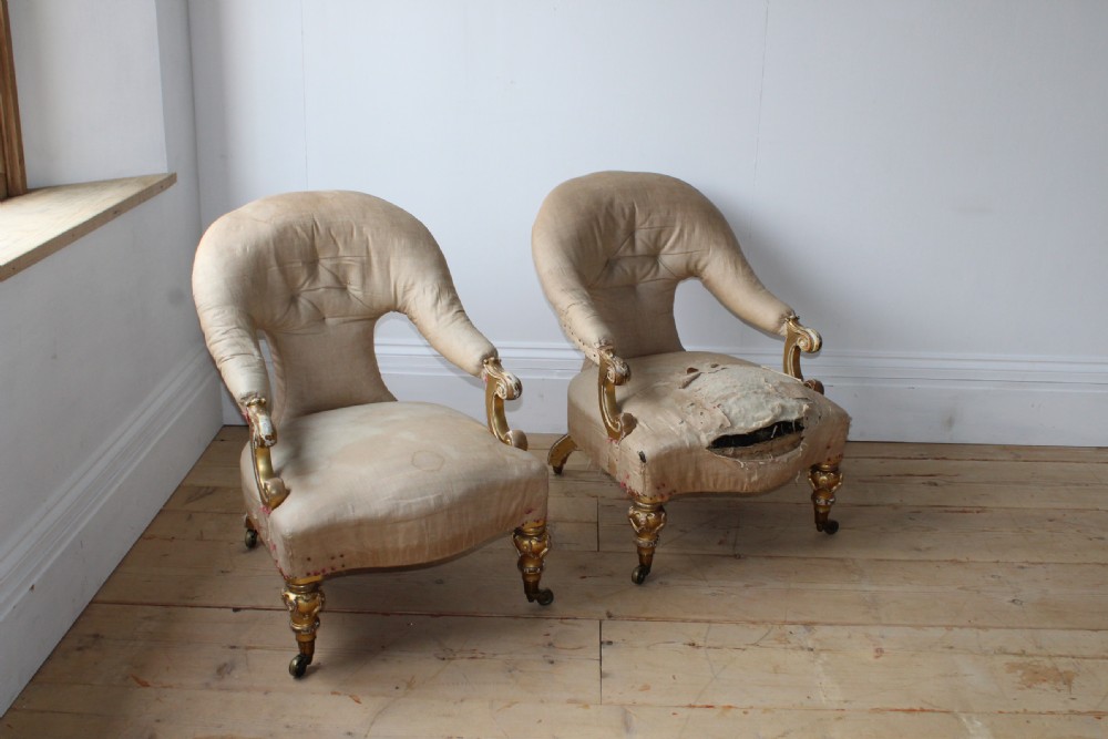 A pair of 19th-century upholstered armchairs with carved giltwood legs on brass castors and cream fabric upholstery.