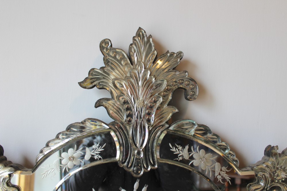 A nineteenth-century Venetian glass wall mirror featuring etched floral motifs, glass rosette fasteners, and a decorative foliate crest. View V