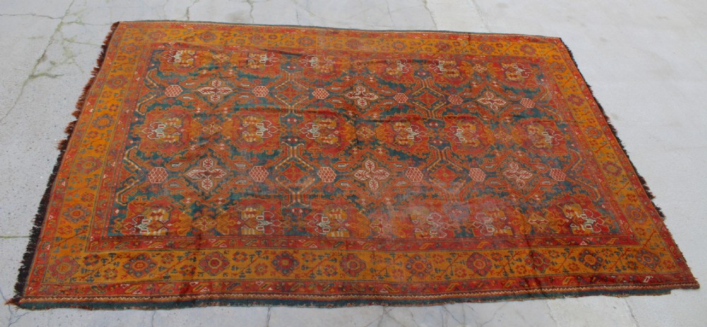 An antique hand-knotted Turkish Ushak wool rug featuring geometric motifs and intricate borders in terracotta, teal, yellow, and saffron tones.