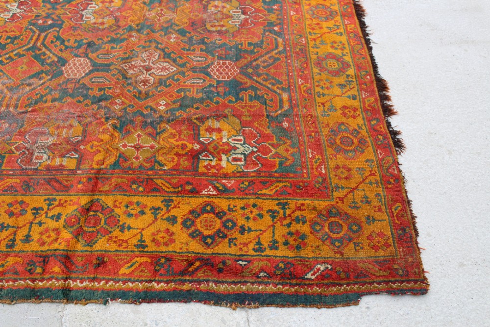 An antique hand-knotted Turkish Ushak wool rug featuring geometric motifs and intricate borders in terracotta, teal, yellow, and saffron tones. View II