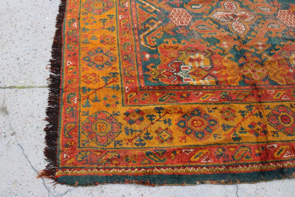 An antique hand-knotted Turkish Ushak wool rug featuring geometric motifs and intricate borders in terracotta, teal, yellow, and saffron tones. View III