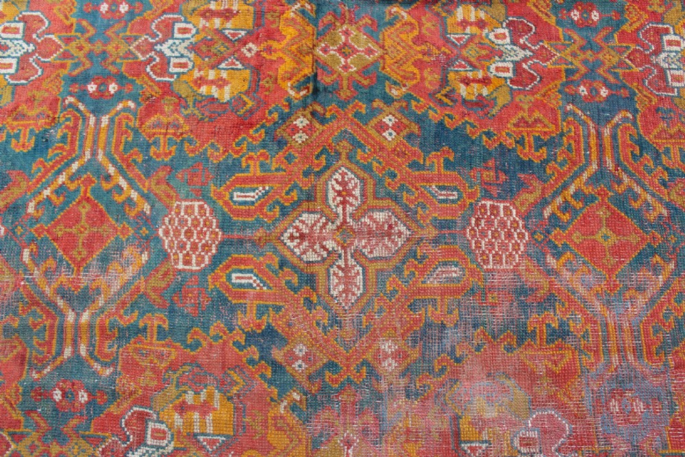 An antique hand-knotted Turkish Ushak wool rug featuring geometric motifs and intricate borders in terracotta, teal, yellow, and saffron tones. View IV
