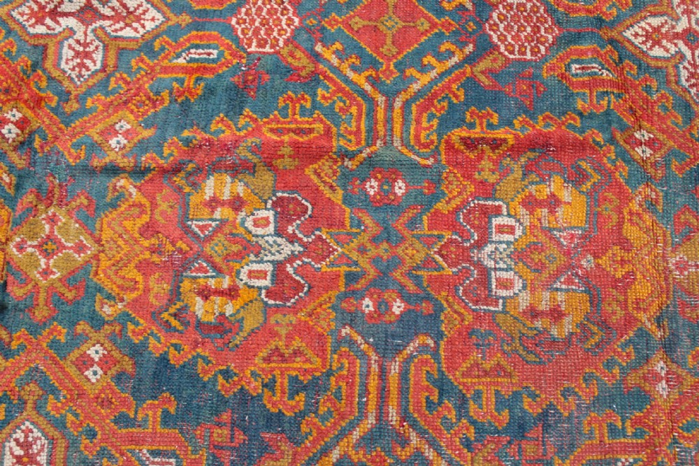 An antique hand-knotted Turkish Ushak wool rug featuring geometric motifs and intricate borders in terracotta, teal, yellow, and saffron tones. View V