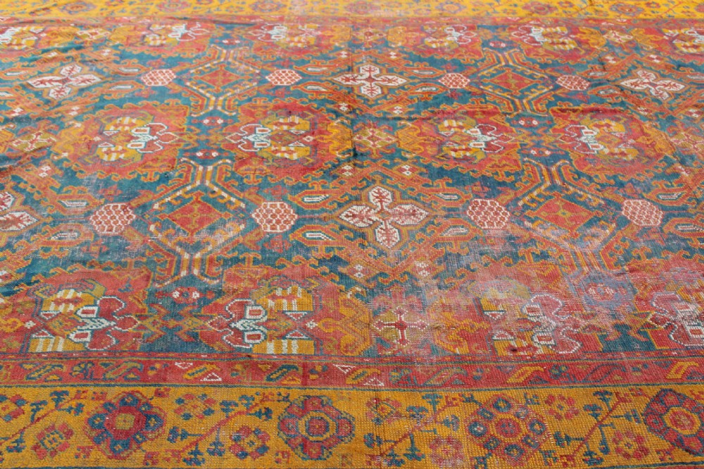 An antique hand-knotted Turkish Ushak wool rug featuring geometric motifs and intricate borders in terracotta, teal, yellow, and saffron tones. View VI