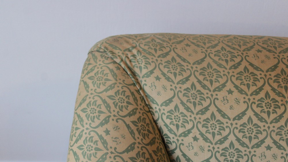 A 20th-century Howard and Sons style two-seater sofa upholstered in sage green patterned fabric with tapered wood legs on brass castors. View IV