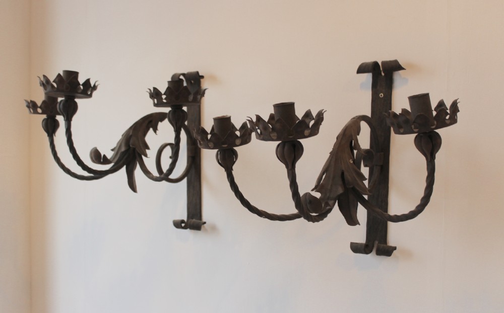 A pair of dark wrought iron Gothic wall lights featuring three twisted branches, coronet-style candle cups, and carved foliate detailing.