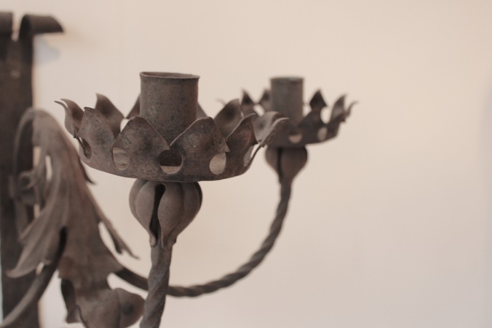 A pair of dark wrought iron Gothic wall lights featuring three twisted branches, coronet-style candle cups, and carved foliate detailing. View VI