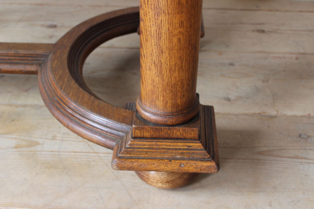 A 19th-century Arts and Crafts oak library table featuring four turned column legs, carved corner brackets, and a curved stretcher base. View V