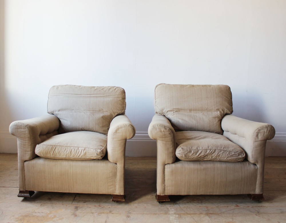 A matching pair of 1920s upholstered lounge armchairs featuring scrolled arms, cushioned seats, beige striped fabric, and low wooden feet.